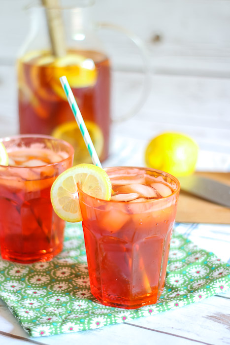 Closeup glass with sun tea and lemon slice with pitcher in background